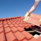 Roof repair, worker with yellow gloves replacing red tiles or shingles on house with blue sky as background and copy space.